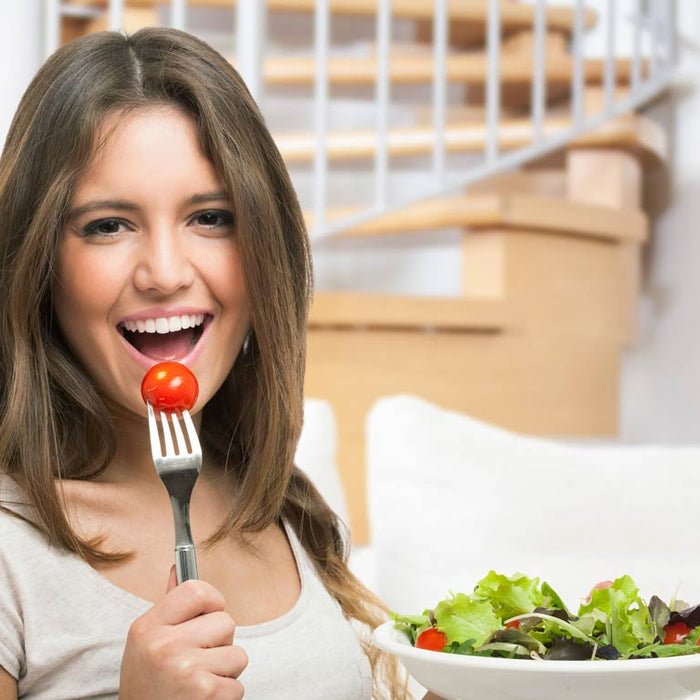 Woman eating a tomato with a bowl of salad